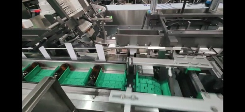 Actual cartoning equipment with amber bottles held horizontally on a green conveyor