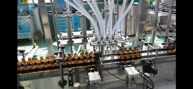 Actual multi-head filling machine with silicone feed tubes and upright amber bottles on the conveyor
